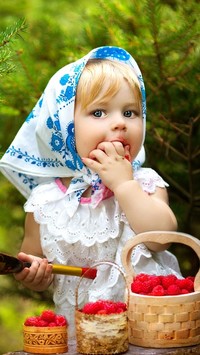 Dziewczynka w chuście zajadająca maliny z koszyczka