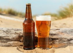 Butelka z szklanką piwa na piasku