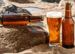 Butelki i szklanka piwa na kamieniu i piasku