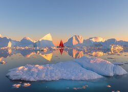 Czerwona żaglówka na morzu obok gór lodowych