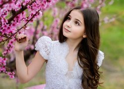 Długowłosa dziewczynka obok kwitnących gałązek