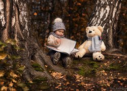 Dziecko z książką i pluszakiem w lesie