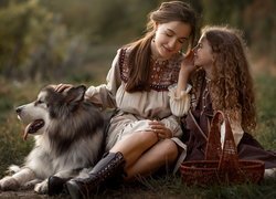 Dziewczynka i kobieta siedzące na trawie z psem