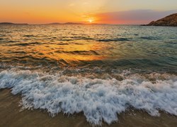 Fale na brzegu morza w blasku zachodzącego słońca