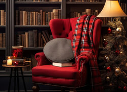 Fotel z poduszką i kocem obok choinki i lampy na tle regału z książkami
