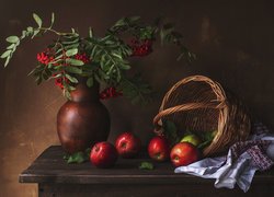 Jarzębina w wazonie obok jabłek i koszyka