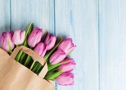 Jasnofioletowe tulipany w papierowej torbie na deskach