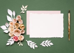 Kartki papieru obok pióra i papierowych kwiatów na zielonym tle