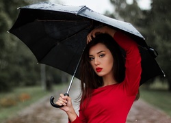 Kobieta w czerwonej bluzce pod parasolem na deszczu