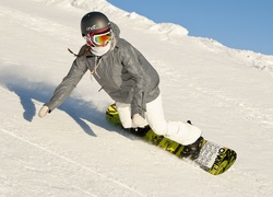 Kobieta zjeżdża z ośnieżonej góry na desce snowboardowej