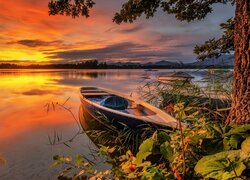 Łódki na brzegu jeziora na tle zachodzącego słońca