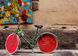 Rower z kołami w kształcie arbuza pod ścianą z obrazem