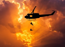 Śmigłowiec Bell UH-1 Iroquois i żołnierze opuszczający się na linach w świetle zachodzącego słońca