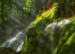 Wodospad na omszonej skale w promieniach światła