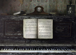 Zegar, fotografia oraz książki i nuty położone na zniszczonym pianinie