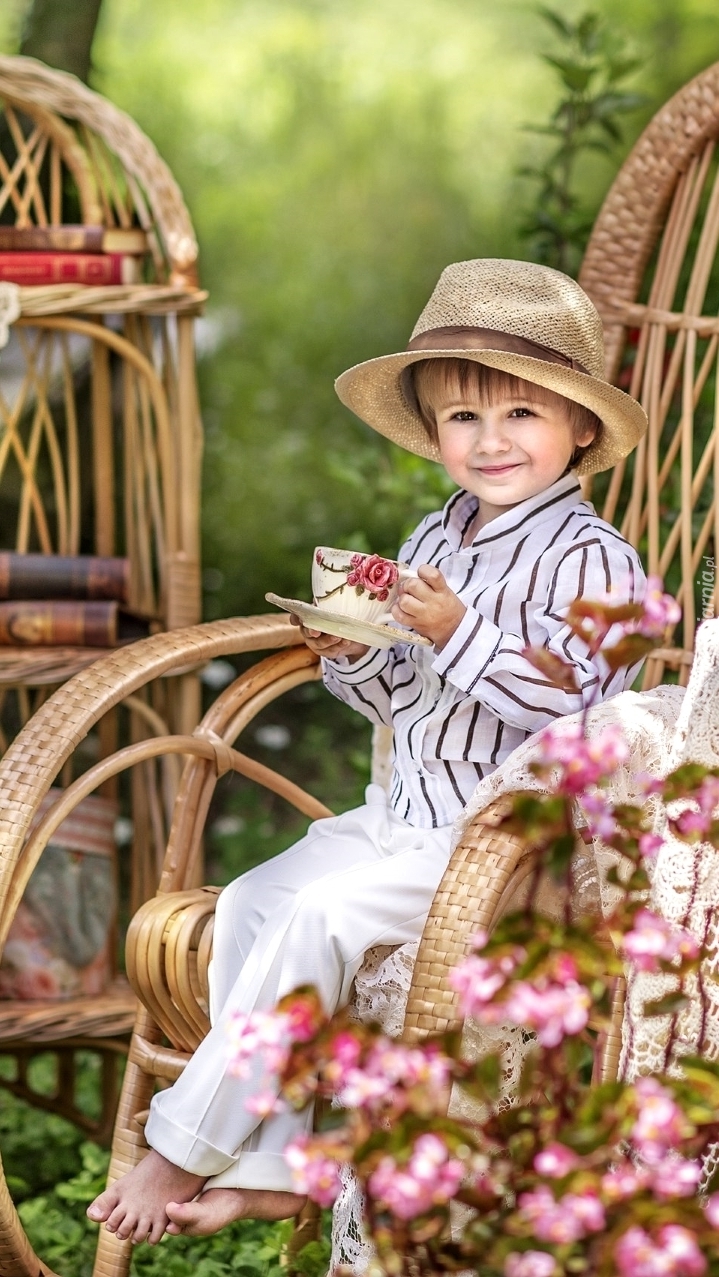 Chłopczyk w kapeluszu na bujanym fotelu z filiżanką