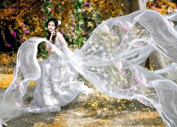 Azjatka w długiej tiulowej sukni na kwiatowej huśtawce w ogrodzie