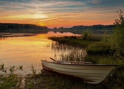 Biała łódka na brzegu jeziora o zachodzie słońca