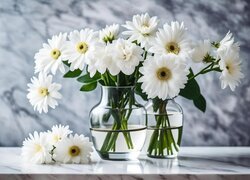 Białe kwiaty w dwóch szklanych wazonach i obok