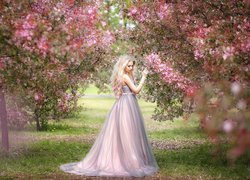 Blondynka w długiej sukni przy drzewie w sadzie