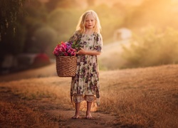 Bosonoga dziewczynka z koszem kwiatów na polnej ścieżce