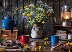 Bukiet kwiatów obok czajnika lampy i kubków do kawy