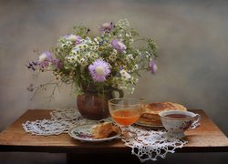 Bukiet kwiatów w glinianym dzbanku obok naleśników i filiżanki herbaty