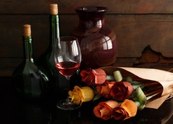 Butelki i kieliszek z winem obok bukietu róż