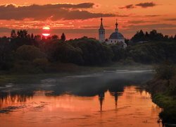 Cerkiew wśród drzew nad rzeką o zachodzie słońca