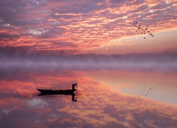 Człowiek w łódce i lecące ptaki w lustrzanym odbiciu jeziora