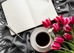 Długopis na zeszycie obok filiżanki z kawą i tulipanów