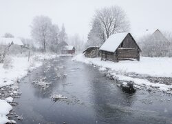 Domy i drzewa w śniegu nad zamarzniętą rzeką