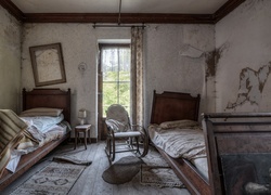 Dwa łóżka i bujany fotel w starej zniszczonej sypialni