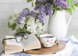 Dzbanek z bzem obok kawy i okularów na książce