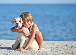 Dziecko na plaży przytulone do szczeniaka rasy labrador retriever