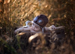 Dziecko w czapce pilotce siedzące w drewnianej skrzynce
