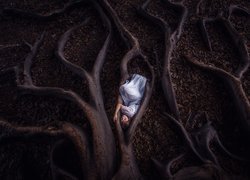 Dziewczyna leżąca pomiędzy korzeniami drzewa