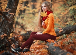 Dziewczyna w swetrze z listkiem w ręce pozuje w jesiennym lesie