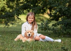 Dziewczynka i szczeniak golden retriever na trawie pod drzewem