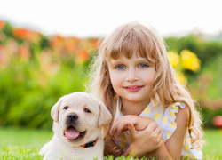 Dziewczynka i szczeniak labradora leżą na kwiatowej łące