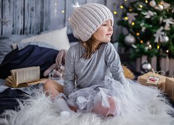 Dziewczynka w czapce siedząca obok prezentów