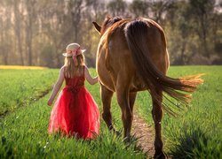 Dziewczynka w czerwonej sukience i kapeluszu obok konia
