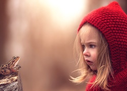 Dziewczynka w czerwonym sweterku z kapturem przygląda się żabce