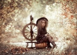 Dziewczynka w kapeluszu siedząca na dyni przy kołowrotku