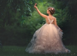 Dziewczynka w tiulowej sukience dotyka gałązki drzewa z motylem