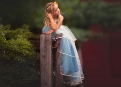 Dziewczynka w tiulowej sukience siedzi na drewnianym płocie