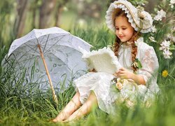 Dziewczynka z książką na łące obok parasolki