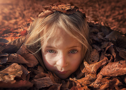 Dziewczynka zasypana jesiennymi liśćmi