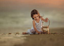 Dziewczynka zbiera na plaży muszelki do słoika
