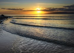 Fale na morzu i kamienie na brzegu o zachodzie słońca